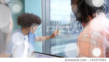 Placing curly-haired man in blue shirt adjusting yellow sticky note on glass at office, copy space Placing curly-haired man in blue shirt adjusting yellow sticky note on glass at office, copy space 141072081