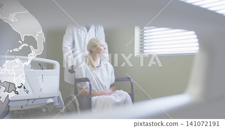 Sitting patient in hospital gown looking at blinds in clinic, doctor in lab coat holding wheelchair Sitting patient in hospital gown looking at blinds in clinic, doctor in lab coat holding wheelchair 141072191
