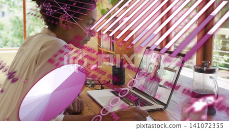 Working mature woman wearing light top writing notes at wooden table, using laptop call overlays 141072355
