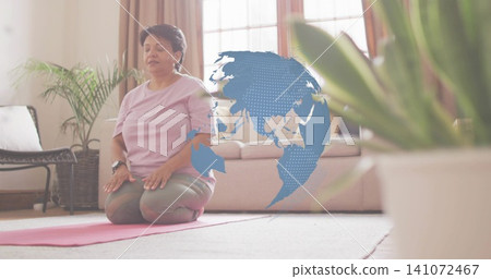 Kneeling senior Indian woman meditating at home on pink mat, wearing purple shirt olive leggings Kneeling senior Indian woman meditating at home on pink mat, wearing purple shirt olive leggings 141072467