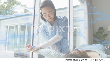 Guiding female therapist in blue scrubs holding patient's wrist on exam table near glass doors, HUD Guiding female therapist in blue scrubs holding patient's wrist on exam table near glass doors, HUD 141072500