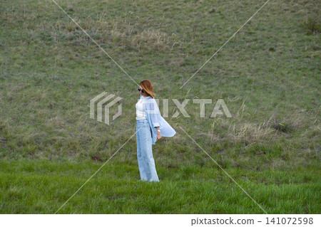 Woman Walking in a Green Field on Rolling Hills, Embracing Freedom and Nature Woman Walking in a Green Field on Rolling Hills, Embracing Freedom and Nature 141072598