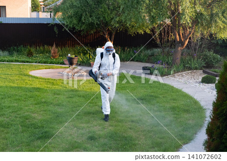 Spring garden pest control: man in protective suit spraying plants 141072602