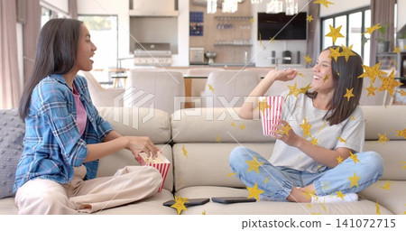 Chatting parent plaid, teen striped holding popcorn on beige sofa at home, gold confetti, remotes Chatting parent plaid, teen striped holding popcorn on beige sofa at home, gold confetti, remotes 141072715