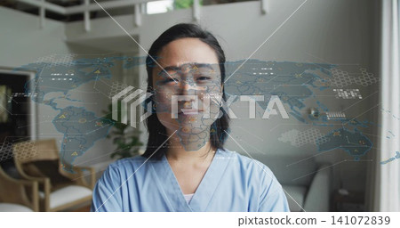 Standing Asian woman wearing light blue scrubs in home loft, AR world map overlaying chest Standing Asian woman wearing light blue scrubs in home loft, AR world map overlaying chest 141072839