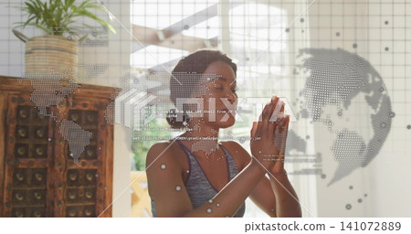 Praying woman in gray athletic tank pressing hands at chest at home with dotted map overlay Praying woman in gray athletic tank pressing hands at chest at home with dotted map overlay 141072889