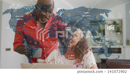 Pointing man redshirt guiding woman floral-top using laptop in kitchen, with digital map and mug 141072902