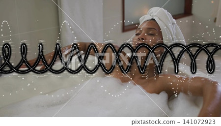 Reclining mid-adult woman soaking in bathroom bathtub with foam, towel-wrapped head, black railing Reclining mid-adult woman soaking in bathroom bathtub with foam, towel-wrapped head, black railing 141072923