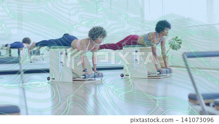 Performing three women supporting weight on pilates chairs in bright studio, wearing athletic wear Performing three women supporting weight on pilates chairs in bright studio, wearing athletic wear 141073096
