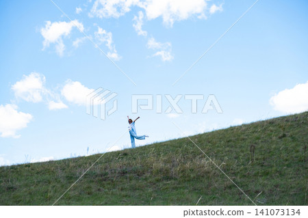 Woman Walking in a Green Field on Rolling Hills, Embracing Freedom and Nature Woman Walking in a Green Field on Rolling Hills, Embracing Freedom and Nature 141073134