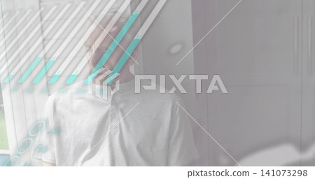 Standing senior man wearing henley shirt near window blinds, showing turquoise glass reflections 141073298