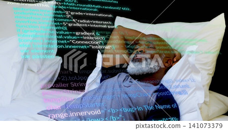 Reclining senior man wearing gray tee on bed with white pillows, resting and viewing projected code Reclining senior man wearing gray tee on bed with white pillows, resting and viewing projected code 141073379