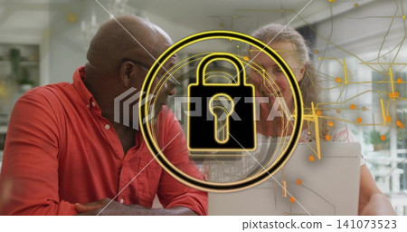 Leaning red-shirted man and patterned-blouse woman using laptop at home, with gold padlock overlay Leaning red-shirted man and patterned-blouse woman using laptop at home, with gold padlock overlay 141073523