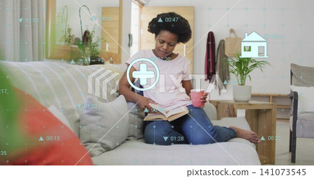 Reading woman in pale pink shirt, jeans on sofa at home holding pink mug, book, HUD Reading woman in pale pink shirt, jeans on sofa at home holding pink mug, book, HUD 141073545