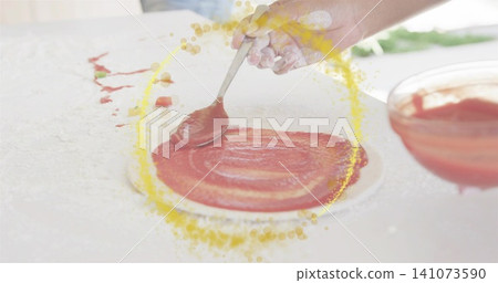 Spreading hand spooning sauce over pizza crust on floured worktop near window, bowl and tomato bits Spreading hand spooning sauce over pizza crust on floured worktop near window, bowl and tomato bits 141073590