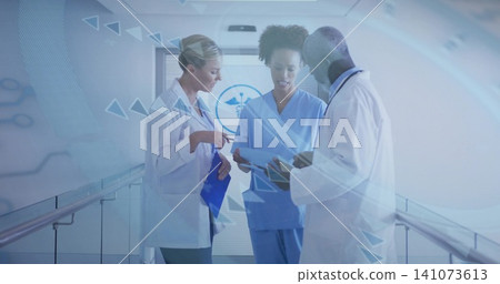 Reviewing charts team in lab coats, scrubs in hospital corridor with blue clipboard tablet emblem Reviewing charts team in lab coats, scrubs in hospital corridor with blue clipboard tablet emblem 141073613