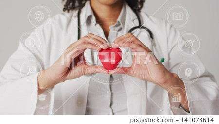 Holding adult clinician showing red heart with laptop icon in clinic in white coat and stethoscope Holding adult clinician showing red heart with laptop icon in clinic in white coat and stethoscope 141073614