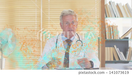 Gesturing senior doctor in white coat at clinic desk, showing stethoscope, fan, teal-orange overlay Gesturing senior doctor in white coat at clinic desk, showing stethoscope, fan, teal-orange overlay 141073619