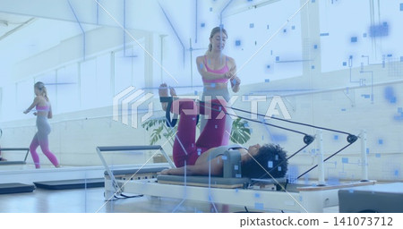 Adjusting instructor in pink guiding client on Pilates reformer at studio, with straps and mirror Adjusting instructor in pink guiding client on Pilates reformer at studio, with straps and mirror 141073712