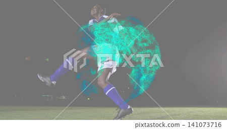 Leaping soccer player in white-blue kit kicking on pitch at night under floodlight, with teal globe 141073716