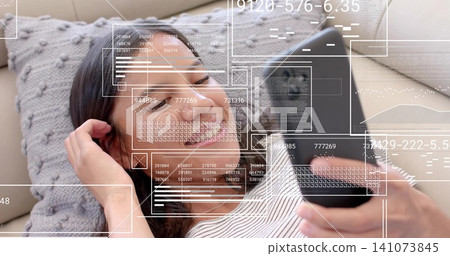 Smiling woman reclining on pale knit sofa cushion, holding phone with HUD, striped tee and bracelet Smiling woman reclining on pale knit sofa cushion, holding phone with HUD, striped tee and bracelet 141073845