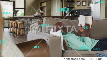 Reclining senior man wearing mint shirt and dark pants, reading book at home with currency overlays Reclining senior man wearing mint shirt and dark pants, reading book at home with currency overlays 141073859