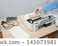 Woman Cleaning and Servicing a Disassembled Home Inkjet Printer on Wooden Desk 141073981