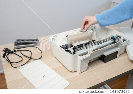 Woman Cleaning and Servicing a Disassembled Home Inkjet Printer on Wooden Desk Woman Cleaning and Servicing a Disassembled Home Inkjet Printer on Wooden Desk 141073981
