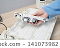 Hand Holding Printer Scanner Carriage During Office Scanner Repair And Maintenance On Desk 141073982