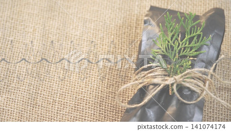 Displaying black wrapped parcel with jute twine, green sprig and metal coil on burlap, copy space Displaying black wrapped parcel with jute twine, green sprig and metal coil on burlap, copy space 141074174