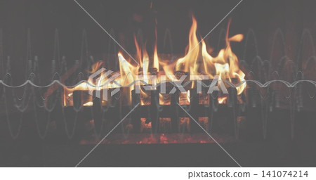 Flickering flames in home fireplace with metal grate, charred logs, embers, and waveform overlay 141074214