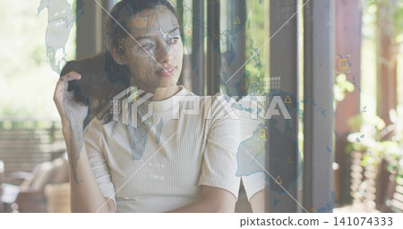 Standing woman in light ribbed top, gazing through glass door at patio with world map overlay Standing woman in light ribbed top, gazing through glass door at patio with world map overlay 141074333