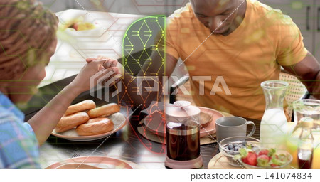 Holding hands family eating meal at home table with bagels, coffee, orange shirt, circuit overlay Holding hands family eating meal at home table with bagels, coffee, orange shirt, circuit overlay 141074834