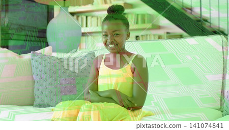 Sitting child in yellow dress folding arms, smiling on living room sofa, with bookshelf pillow lamp 141074841