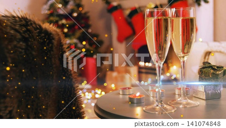 Showing two filled champagne flutes on round table by fireplace, with candles, gift, copy space Showing two filled champagne flutes on round table by fireplace, with candles, gift, copy space 141074848
