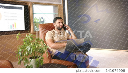Holding smartphone, man wearing beige polo and dark jeans talking in office lounge, laptop on lap Holding smartphone, man wearing beige polo and dark jeans talking in office lounge, laptop on lap 141074906