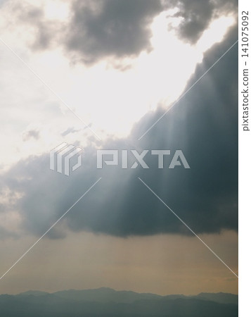 A curtain of light pouring down onto the mountain range through gaps in the clouds, creating a dramatic summer sky. A curtain of light pouring down onto the mountain range through gaps in the clouds, creating a dramatic summer sky. 141075092
