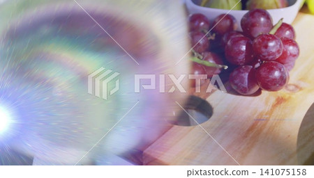 Showing red grape cluster on cutting board at kitchen table, lens flare and bowl, copy space Showing red grape cluster on cutting board at kitchen table, lens flare and bowl, copy space 141075158