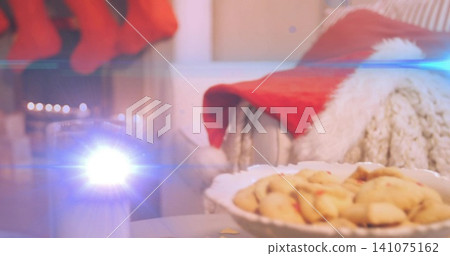 Displaying white scalloped bowl holding cookies on tabletop front, with candle flare and Santa hat Displaying white scalloped bowl holding cookies on tabletop front, with candle flare and Santa hat 141075162