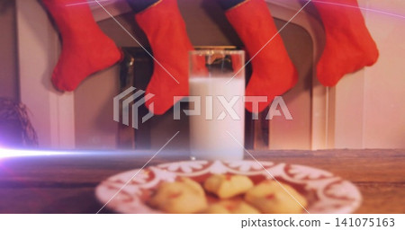 Centering tall glass of milk on table near fireplace, plate of cookies and four red stockings Centering tall glass of milk on table near fireplace, plate of cookies and four red stockings 141075163