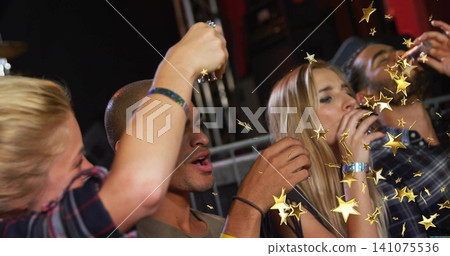 Raising shot glasses, four friends taking shots at club stage with gold stars, wristbands 141075536