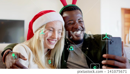 Smiling adult couple taking selfie in living room, with smartphone, Santa hat, antlers, green icons Smiling adult couple taking selfie in living room, with smartphone, Santa hat, antlers, green icons 141075671