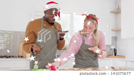 Decorating couple wearing grey aprons and holiday headwear at home kitchen island, with piping bag Decorating couple wearing grey aprons and holiday headwear at home kitchen island, with piping bag 141075677