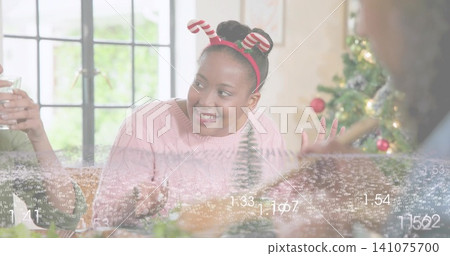Smiling woman in pink sweater and candy-cane headband talking at living room table, numeric overlay Smiling woman in pink sweater and candy-cane headband talking at living room table, numeric overlay 141075700