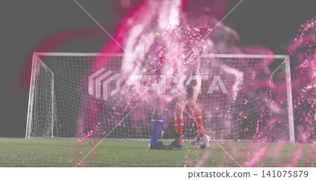 Competing two soccer players vying for ball on grass pitch at night, with goal, pink-smoke, cleats Competing two soccer players vying for ball on grass pitch at night, with goal, pink-smoke, cleats 141075879