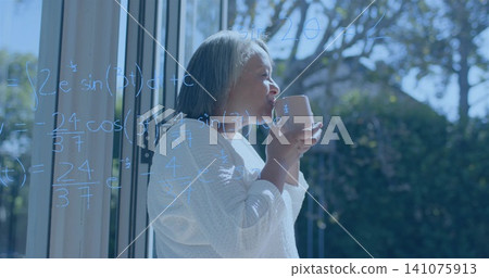 Holding ceramic mug, senior woman in white knit sweater looking through patio door with blue math Holding ceramic mug, senior woman in white knit sweater looking through patio door with blue math 141075913