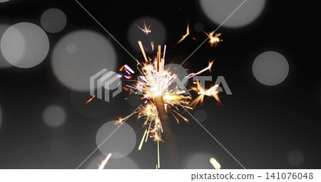 Burning sparkler with metal stem emitting bright sparks against dark backdrop, thin smoke and bokeh Burning sparkler with metal stem emitting bright sparks against dark backdrop, thin smoke and bokeh 141076048