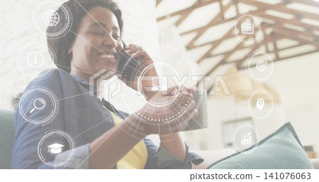 Smiling woman wearing denim shirt holding smartphone and mug on sofa in lounge with HUD icons Smiling woman wearing denim shirt holding smartphone and mug on sofa in lounge with HUD icons 141076063