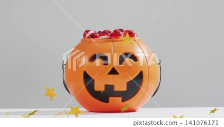 Sitting orange jack o'lantern bucket holding red candies with black loop on studio table gold stars Sitting orange jack o'lantern bucket holding red candies with black loop on studio table gold stars 141076171