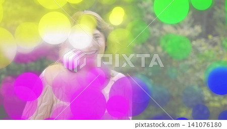 Smiling woman standing in park wearing knit sweater and headband with colored bokeh circles Smiling woman standing in park wearing knit sweater and headband with colored bokeh circles 141076180